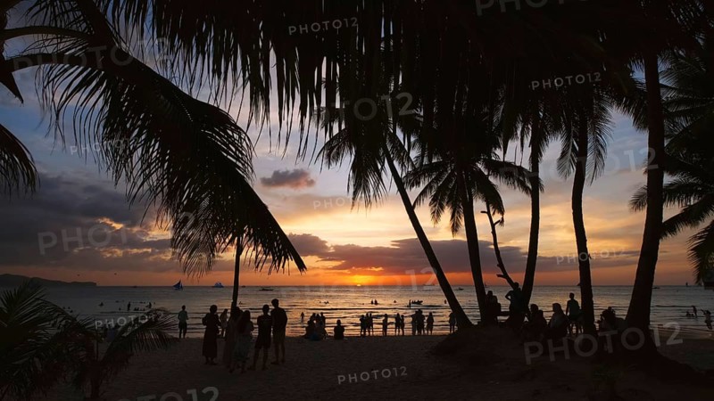 Silhouetted people and palms near sea. Sunset at tropical White beach, Boracay island, Philippines