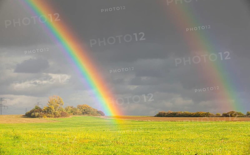 Two natural rainbow over green field after heavy rain