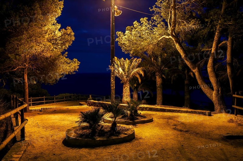 Gloomy square in abandonded park by the sea at midnight illuminated by single lamp, Costa Brava in Lloret de Mar, Catalonia, Spain
