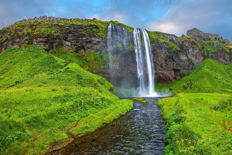 The warm July day in Iceland. Seljalandsfoss waterfall. Rainbow decorates drop of water