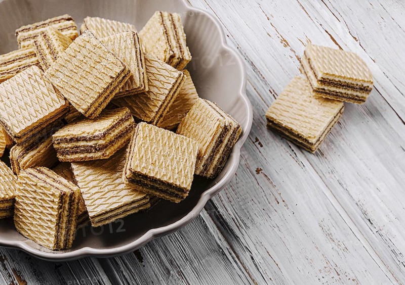 Food, Crisp layered wafers are neatly arranged in a bowl, their patterns creating an inviting look. A few wafers are placed beside the bowl on a rustic wooden table