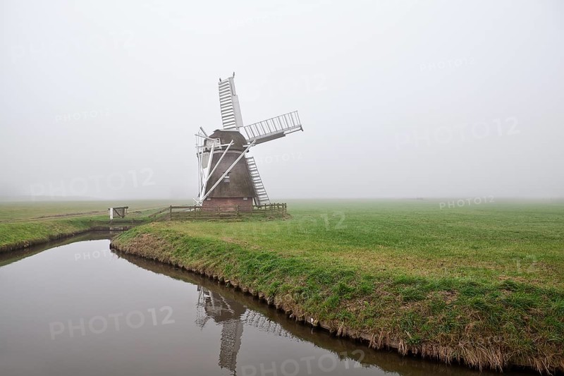 Dutch wooden windmill in fog by canal