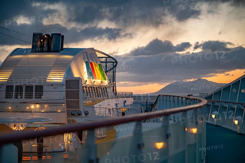 Illuminated AIDA Logo attached to AIDA Bella ship with fence and boat deck in front in the evening