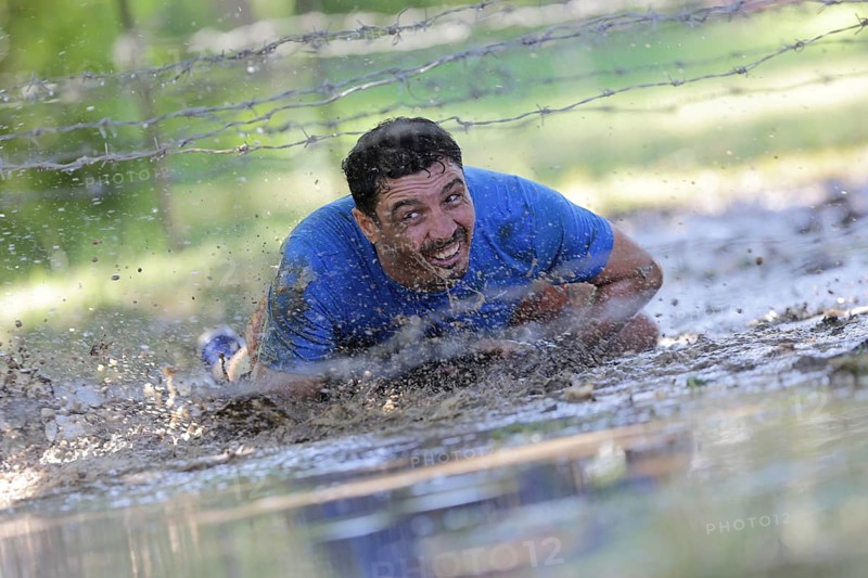 Sofia, Bulgaria - July 9, 2016: A participant is crawling through water under electrified wires at the Legion Run extreme sport challenge near Sofia. The sports event is mud and obstacle course designed to test people's physical strength, stamina, and mental grit
