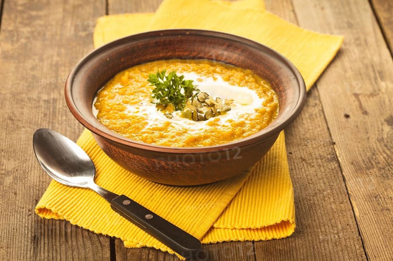 Pumpkin soup in clay bowl with spoon on the table