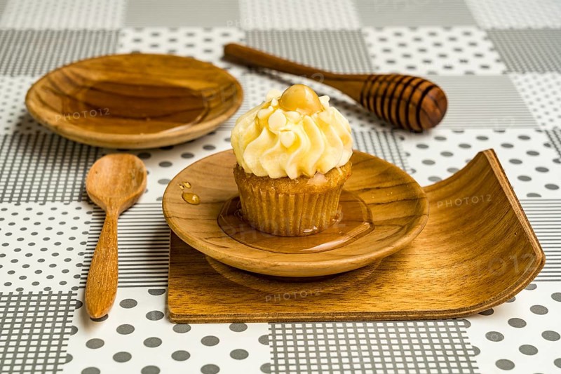 Cupcake and natural honey in a wooden plate with wooden spoon and wooden honey dipper stick