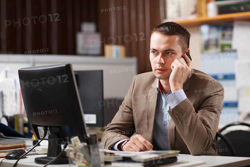 Businessman sitting behind his desk in the office talking on a mobile phone listening to the conversation with a serious expression