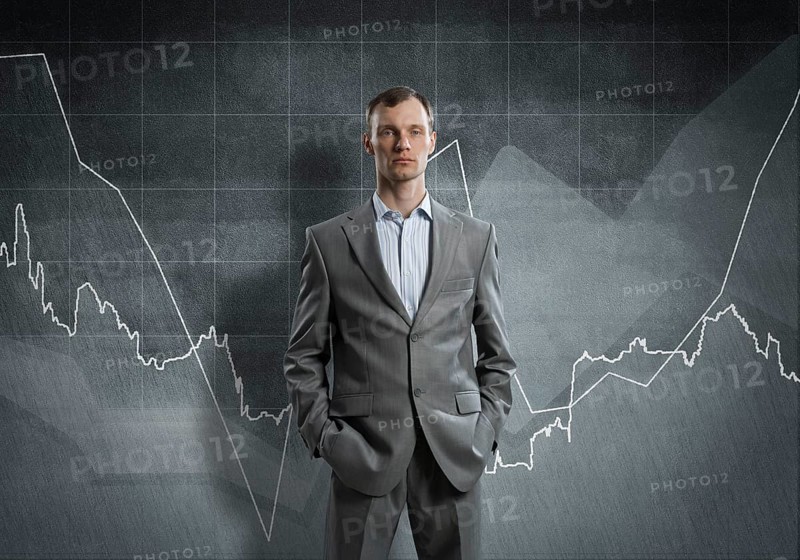 Businessman with arms in pockets and growing graphs on chalkboard