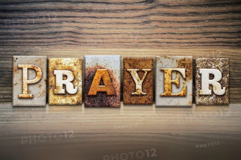 The word PRAYER written in rusty metal letterpress type sitting on a wooden ledge background