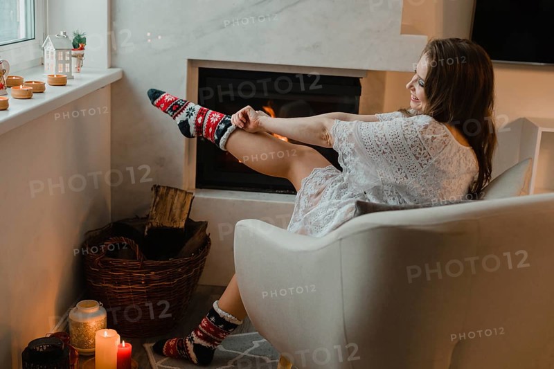 The young girl is sitting in a cozy room by the fireplace. The girl is sitting in an easy chair and dresses warm christmas socks
