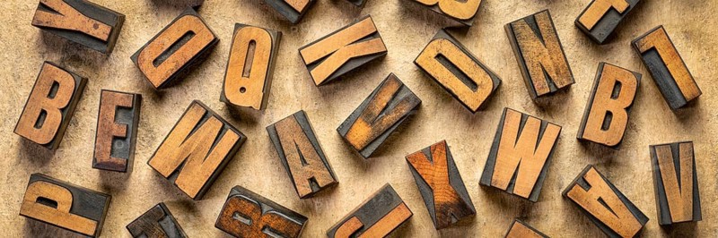 Random letters overhead background - vintage letterpress wood type of different fonts (inverted image) against brown handmade bark paper, panoramic banner