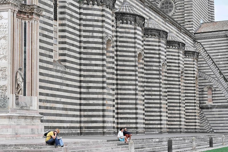 The Cathedral Basilica of Santa Maria Assunta, Orvieto, Terni, Umbria, Italy, People sitting in front of a wall of a historic striped building, Orvieto, Italy