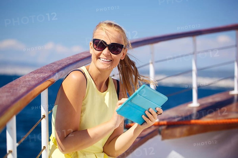 Young smiling woman in sunglasses holding tablet computer and looking somewhere while traveling by ship