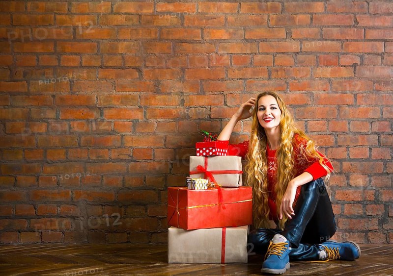 Young woman with Christmas gift near brick wall