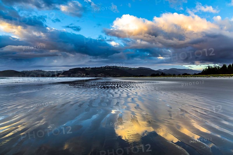 Low tide. Strips of sand and water left by the ocean tide. Sunrise over the ocean. New Zealand, Pacific Coast. The concept of artistic photography. Artistic postal and greeting card
