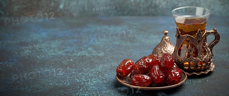 Breaking fasting with dried dates during Ramadan Kareem, Iftar meal with dates and Arab tea in traditional glass, angle view on rustic blue background. Muslim feast, space for text, food photography, food photography