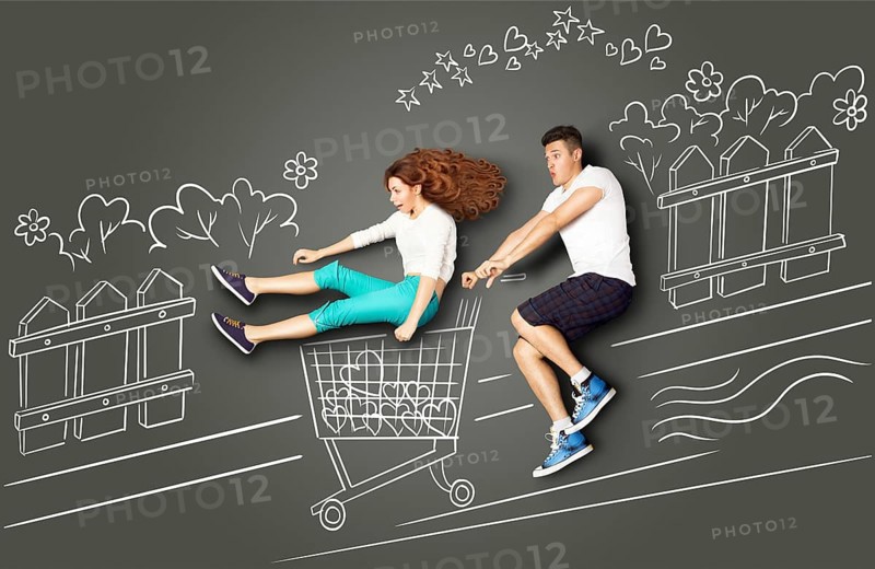 Happy Valentine's Day love story concept of a romantic couple on chalk drawings background. Male riding his girlfriend in a shopping trolley along the street