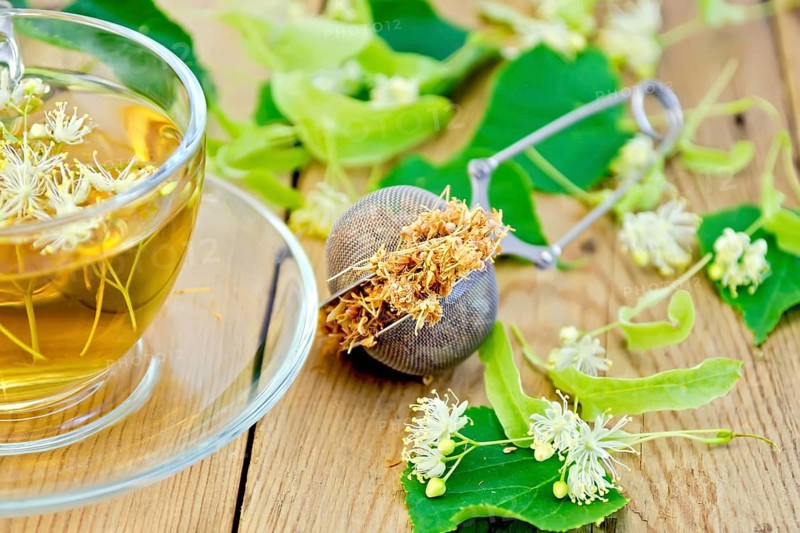Metal sieve with dried flowers of linden, fresh linden flowers, tea in a glass cup on a wooden board