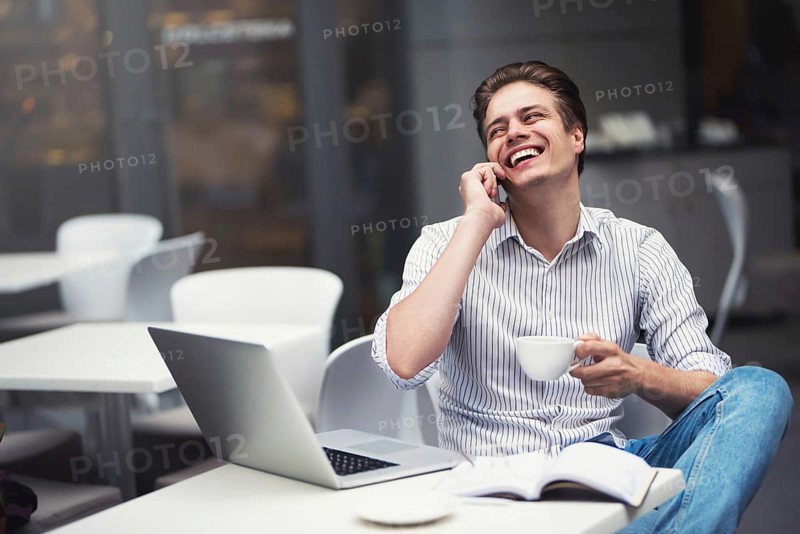 Handsome caucasian young man with phone working on laptop and smiling while enjoying coffee in cafe