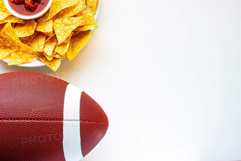 An American football with organic nacho chips and mild salsa on the side on a white background
