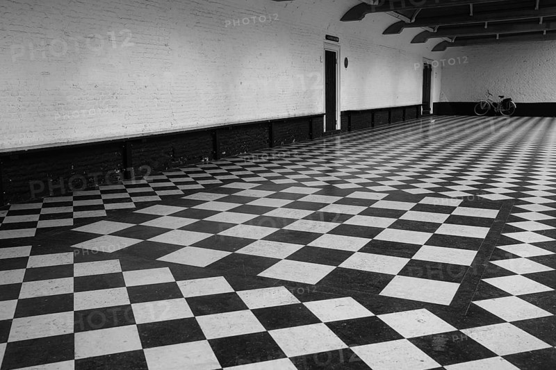Chequered floor covering in front of a white house wall, behind it a vintage bicycle, black and white, Renesse, Netherlands