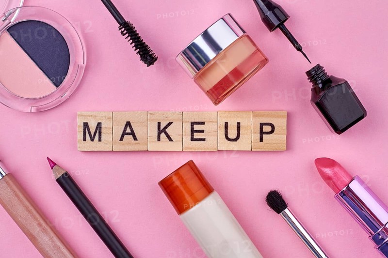 Close up of various female makeup accessories on pink background. Wooden cubes with text makeup