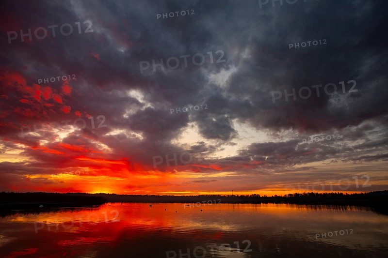 A truly stunning sunset over a calm and reflective lake showcases vibrant hues and dynamic clouds surrounding it