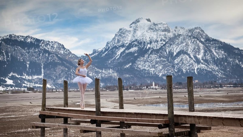 Ballerina dances elegantly on a wooden footbridge in front of snow-covered mountains, in the background the Säuling, Forggensee, Füssen, Allgäu, Bavaria, Germany
