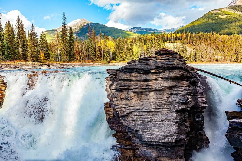 Magnificent rock divides thundering Athabasca Falls. Athabasca Falls is the most powerful waterfall in Alberta. Jasper Park. Canadian Rockies. Picturesque forest illuminated by sunset