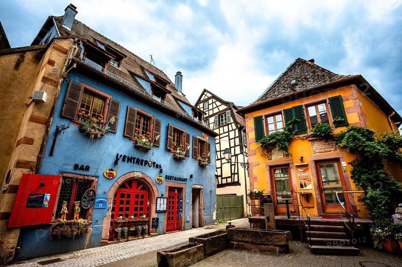 Colourful historic facades with cosy bars and restaurants under a cloudy sky. Alsace France