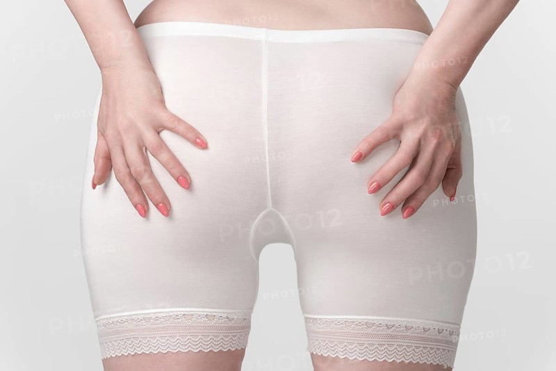 Woman's hips in pantaloons panties, back view of woman with her palms placed on her buttocks. Close-up of the midsection of an unrecognizable plus size female body. Women's health and wellness concept