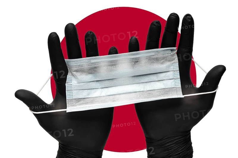 Doctor holds face mask in hands in black medical gloves on background colors flag of flag of Japan or Japanese flag. Pandemic insurance coronavirus, airborne diseases. Human respiratory medical mask