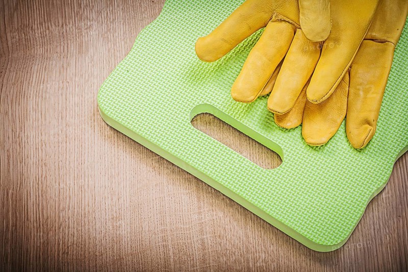 Protective gloves kneeling pad on wooden board gardening concept