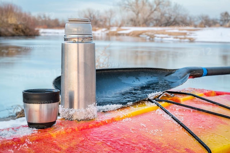 Winter kayaking in Colorado - thermos bottle with hot tea on the icy deck of a red whitewater kayak on shore of St Vrain Creek