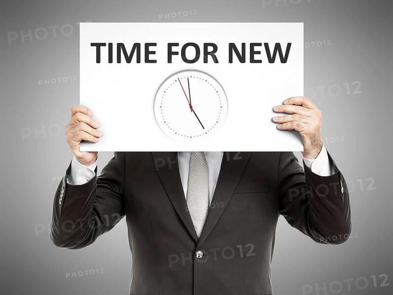A business man holding a paper in front of his face with time for new and a clock