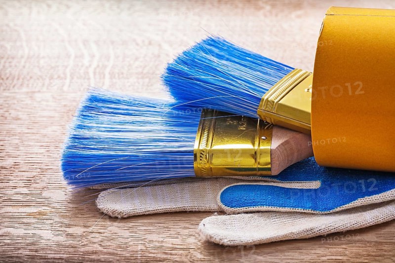 Two paint brushes in roll of duct tape and working gloves on wooden board