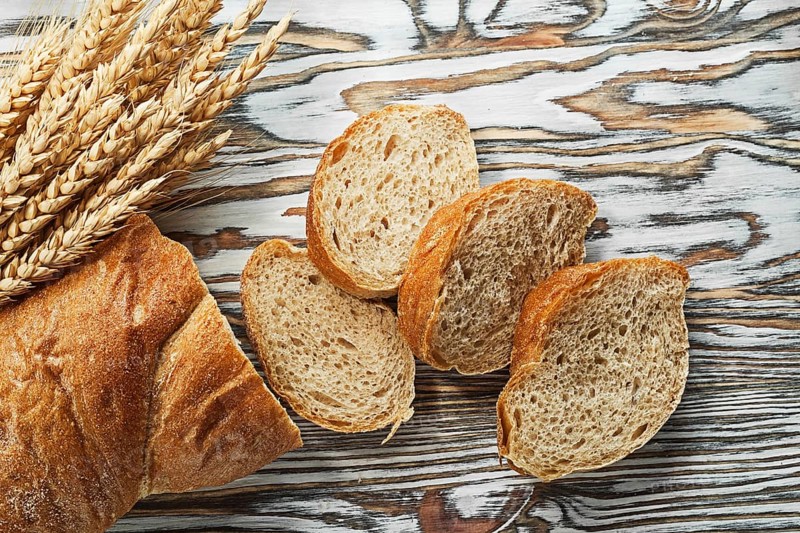 Sliced bread ripe rye ears on wooden surface