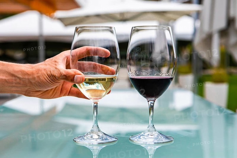 Man hand on white wine glass, pair of white and red wines glasses close up selective focus, restaurant patio outdoor table background