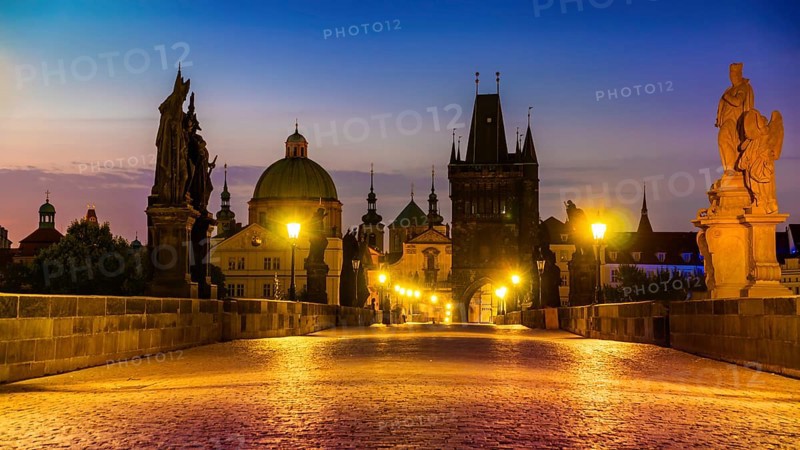 Charles Bridge illuminated with street lights at sunrise, Prague
