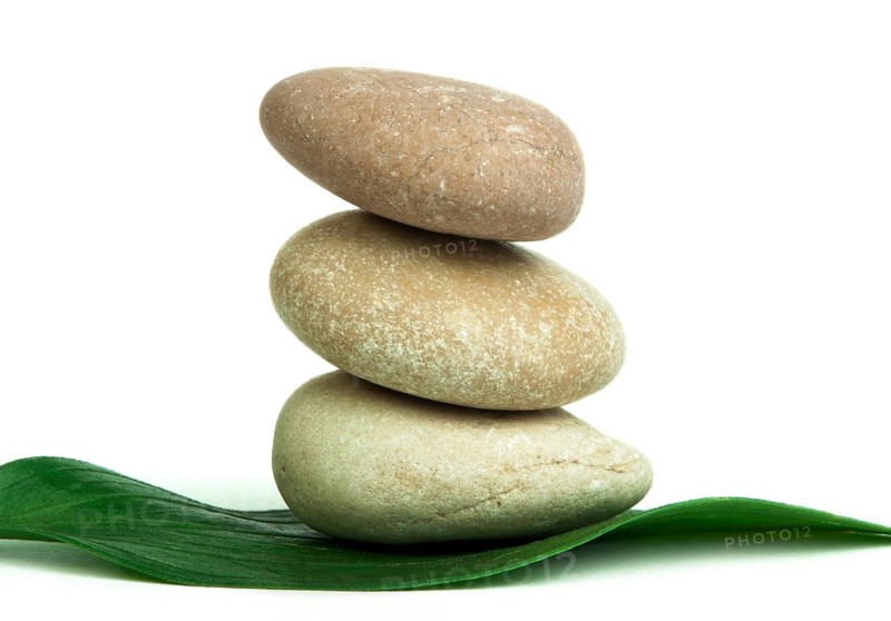 Stacked stones on base of green leafs. White isolated studio shot