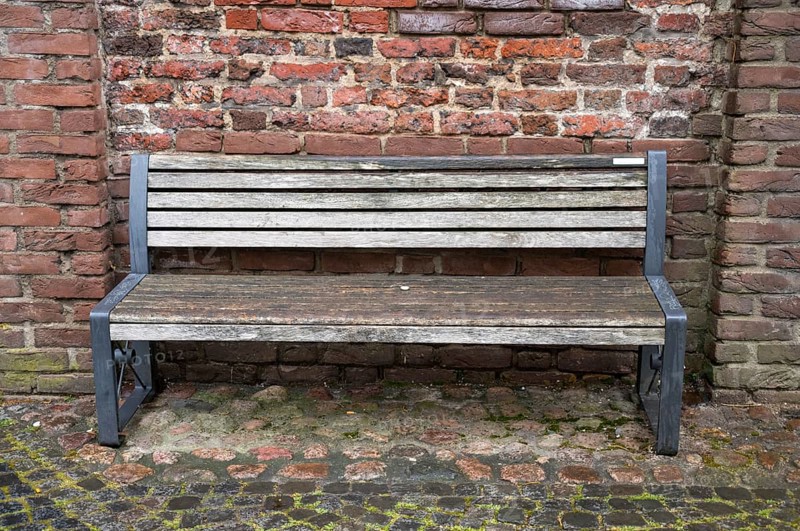 Empty wooden bench with metal frame sits against a weathered brick wall, inviting contemplation and rest