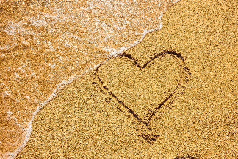 Heart symbol on the sand. Summer holiday concept. Romantic love background. Valentin Day theme. Top view. Heart drawn in sea beach sand, soft wave in a sunny day