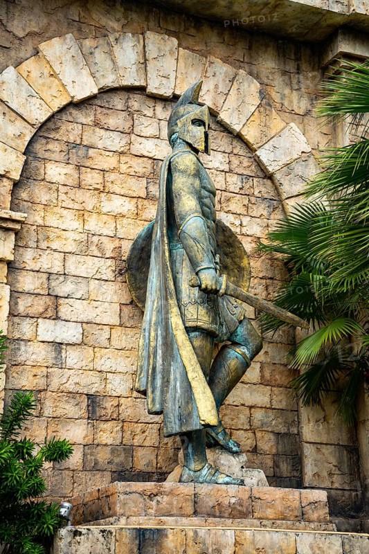 Close-up of an ancient statue with helmet and shield amidst stonework and greenery, palms, city, sun city, Phu Quoc, Vietnam