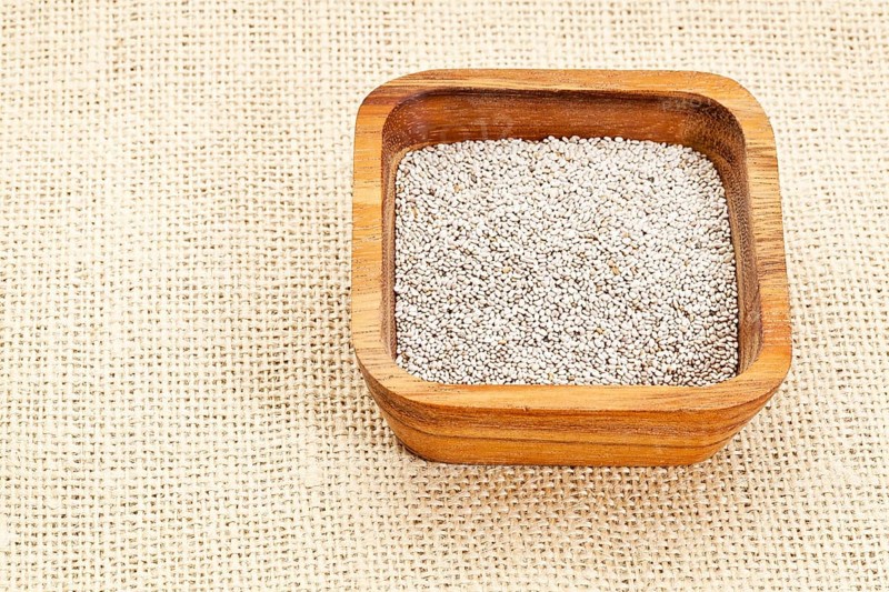 White chia seeds in square wooden bowl against burlap canvas