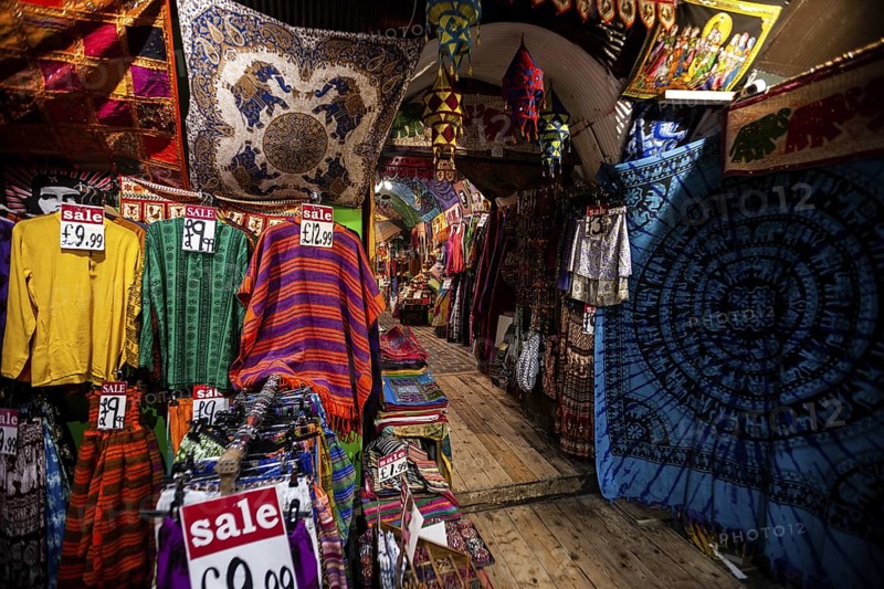 Colorful garments and textiles with sale signs in a vibrant market setting in the London Borough of Camden, Greater London, United Kingdom