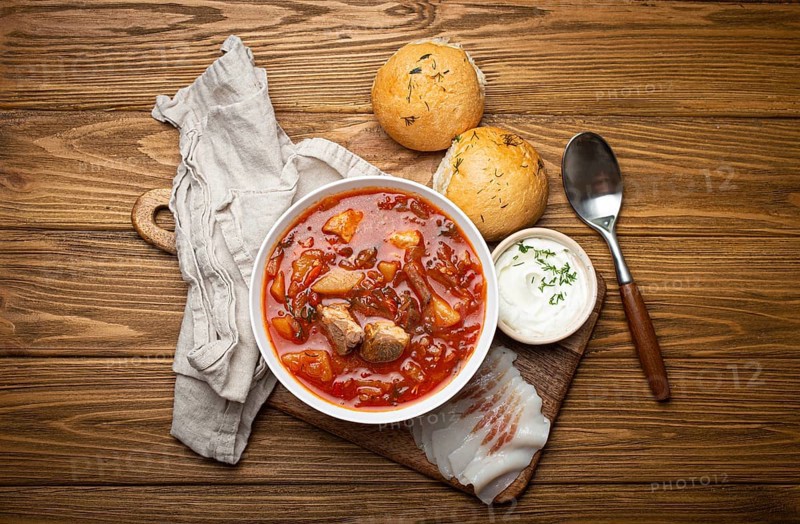 Ukrainian Borscht, red beetroot soup with meat, in white bowl with sour cream, garlic buns Pampushka and salo slices on rustic stone background. Traditional authentic dish of Ukraine, food photography, food photography