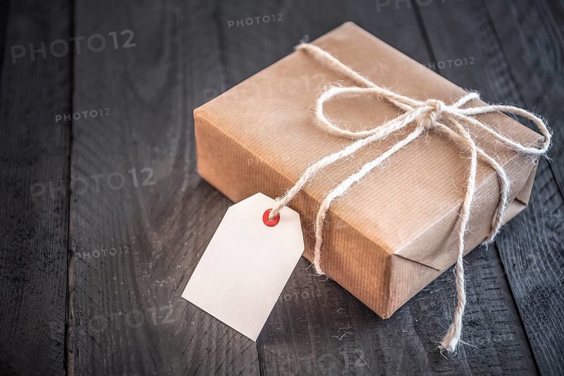 Gift box, wrapped in brown vintage paper and tied with white flax string, on an old black wooden table