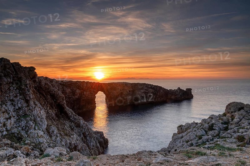 A view of the landmark stone arch of Pont d'en Gil on Menorca Island at sunset