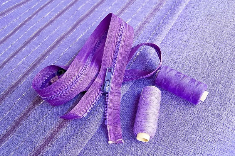 Locking zipper and two reels of thread on the purple plain and striped fabrics