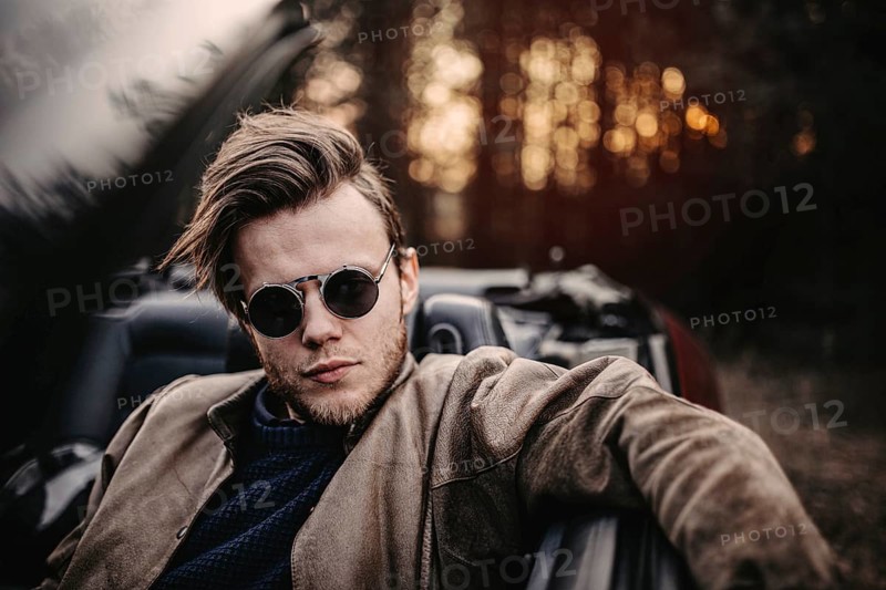 Man with sunglasses in a convertible, pensive mood during sunset
